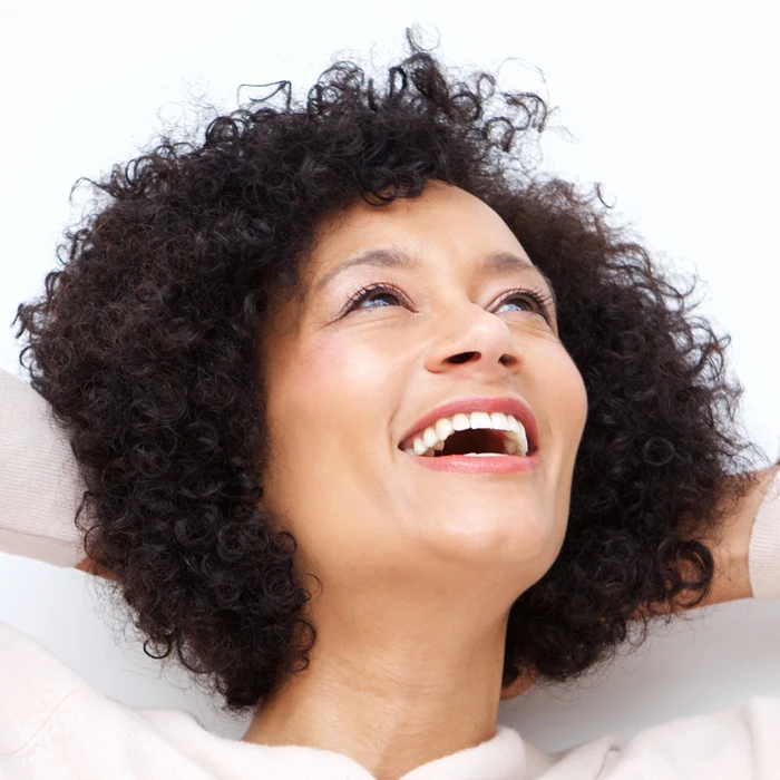Close up portrait of happy older woman laughing with hands behind head against white background
