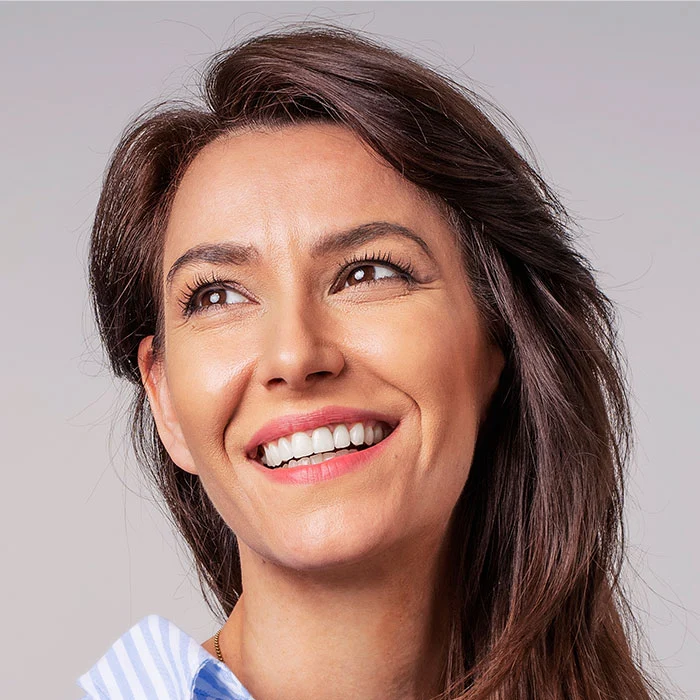 Smiling brunette businesswoman sitting against gray background.