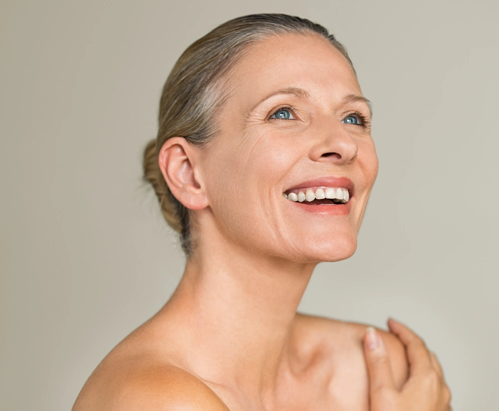 Portrait of a cheerful senior woman smiling while looking away isolated on gray background